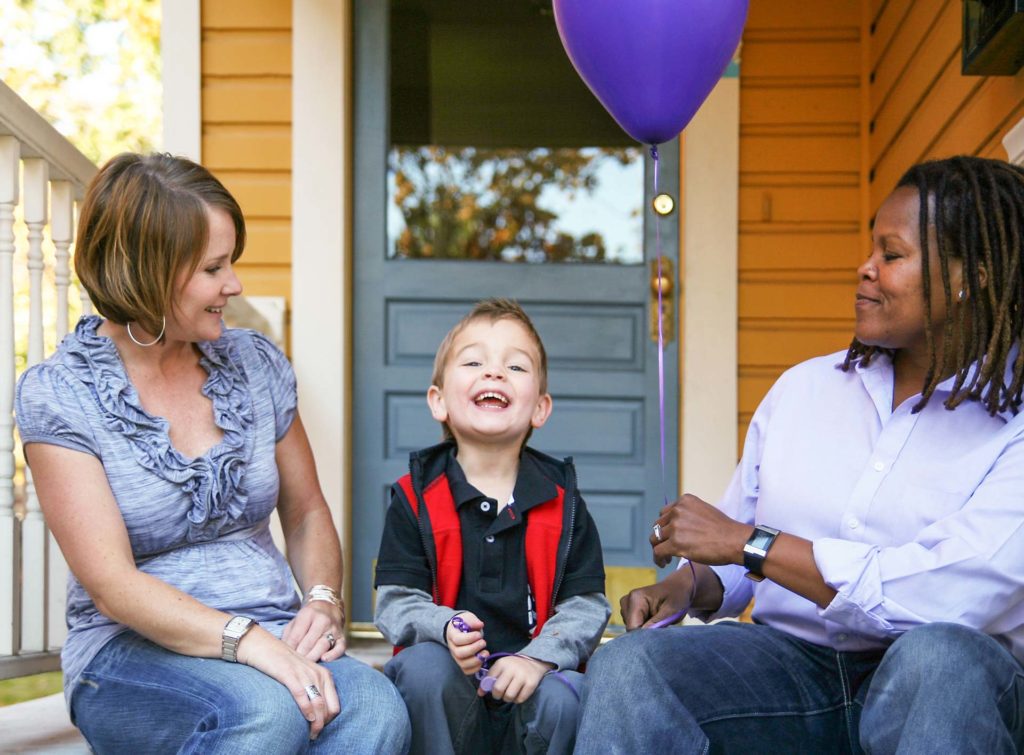 A blended family with a little boy holding a blue balloon, sitting on the front porch.